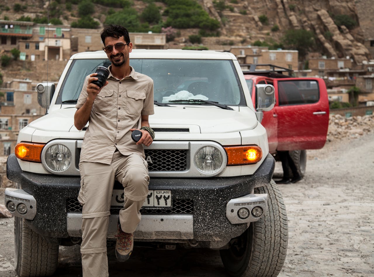 A photographer stands by an SUV holding a camera lens in a rural area.